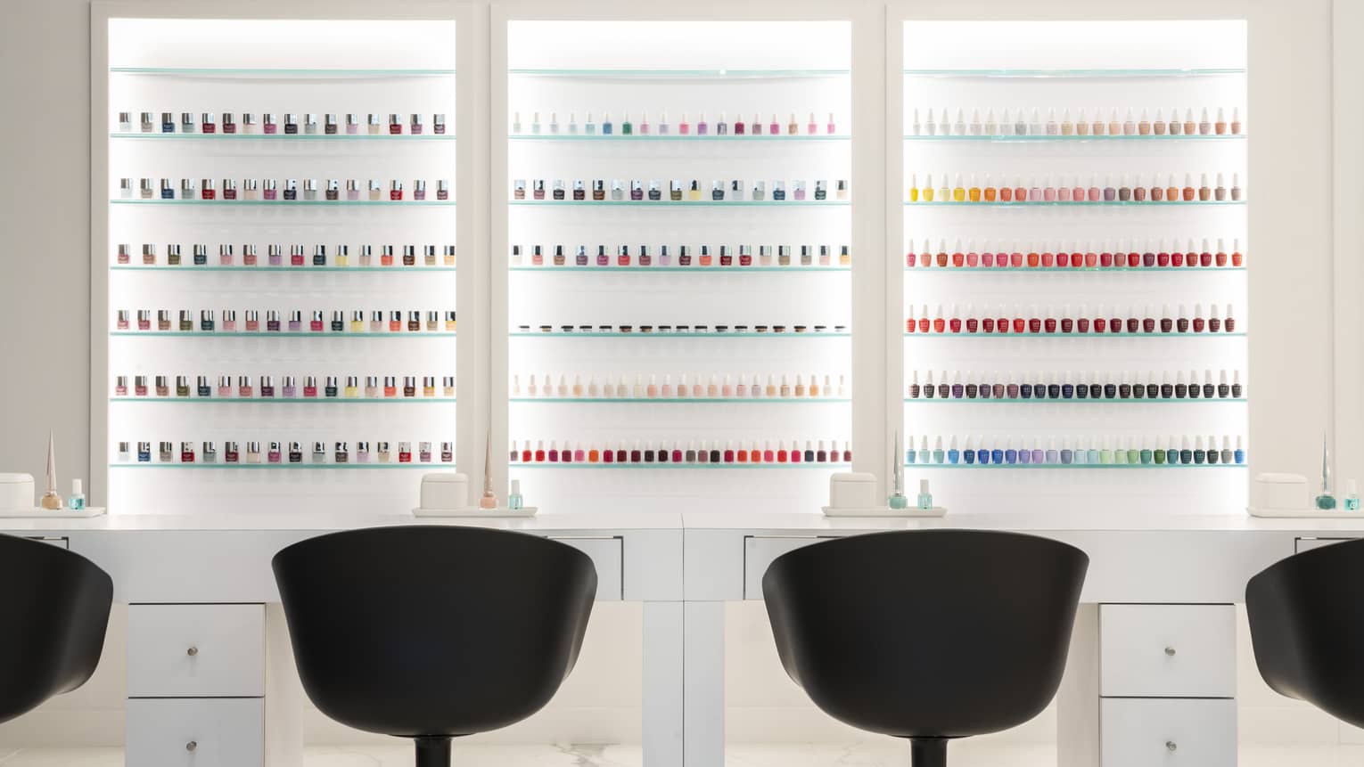 Salon chairs facing an assortment of nail polish in many different colours.