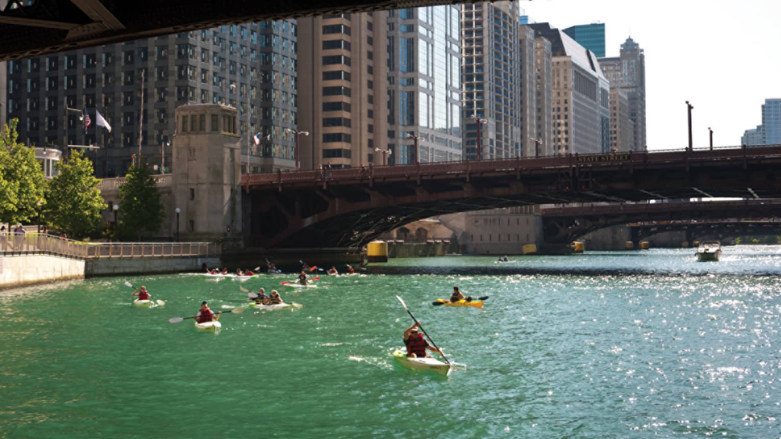 People kayaking on a river under a bridge.