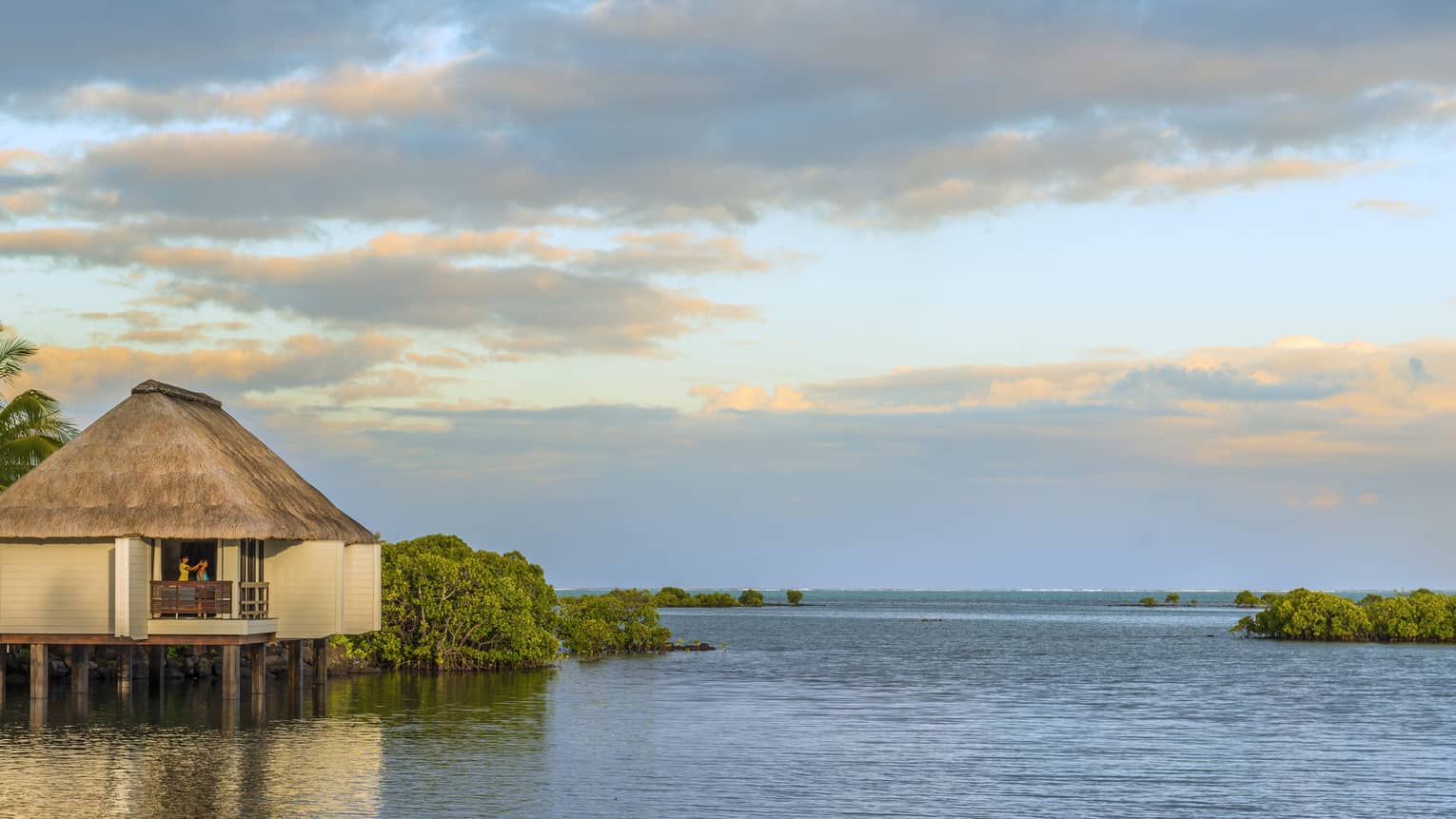 Overwater spa villa with thatched roof at sunrise