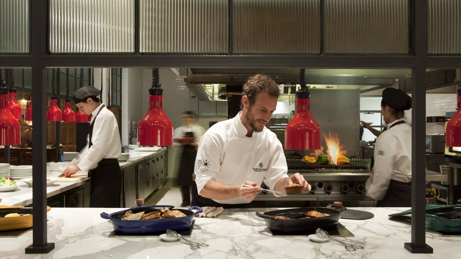 Chefs assemble dishes in a bustling kitchen, lit by red lights