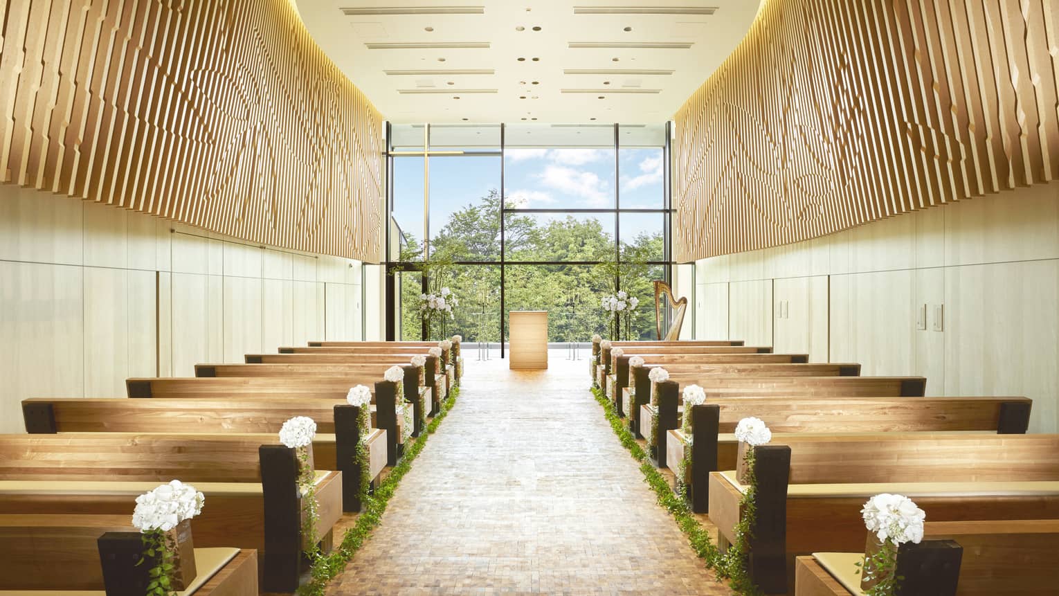 Rows of pews on either side of aisle, floor-to-ceiling window in in bright, modern chapel