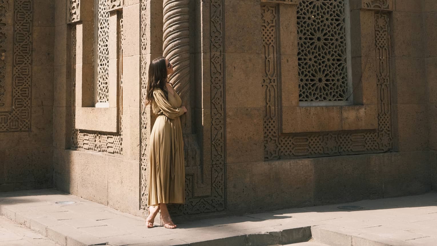 A guest looks up at an ornately carved building featuring a spiral column and arched windows with honeycomb latticework.