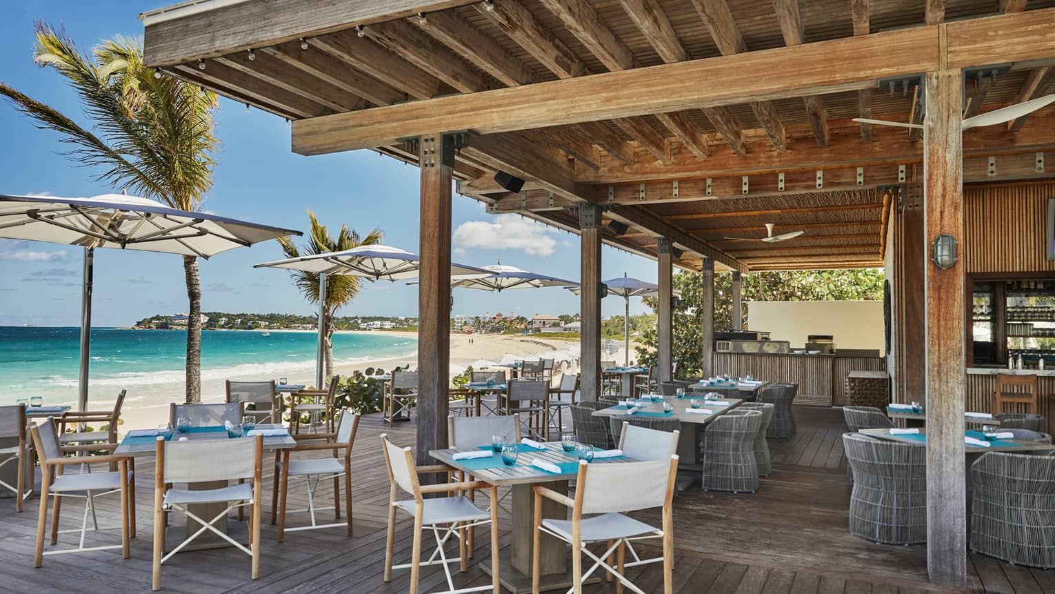 Bamboo restaurant outdoor patio, tables and chairs under wood pergola, beside sunny beach