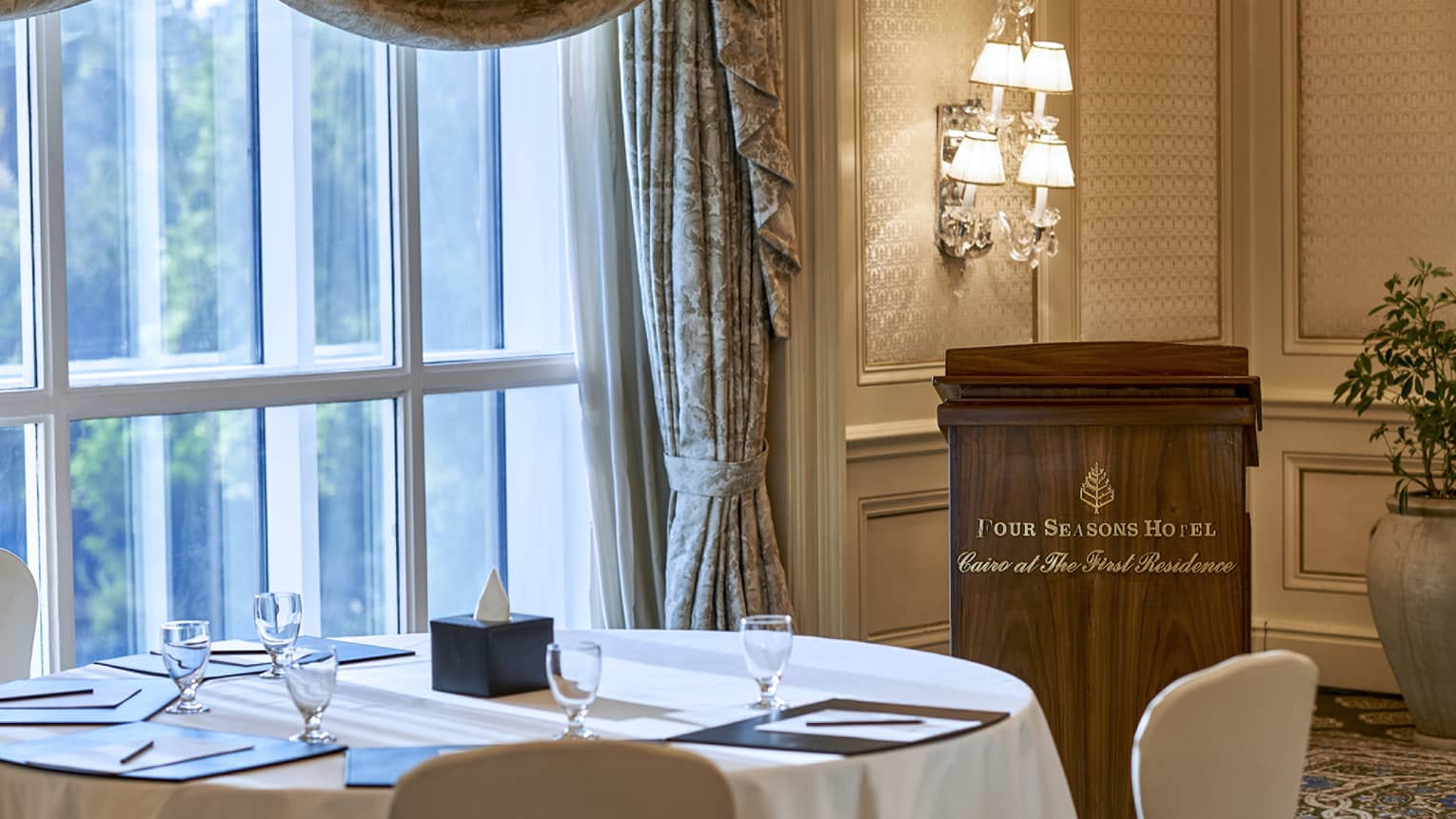 Round table by sunny window, speaker podium with Four Seasons Hotel Cairo at the First Residence logo