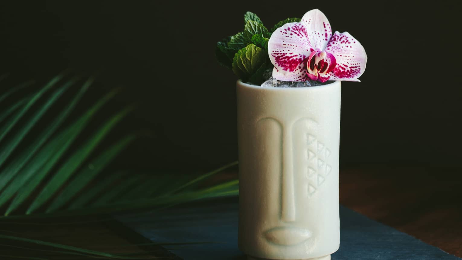 The Talisman cocktail in a tiki shaped glass with fresh flowers as a garnish