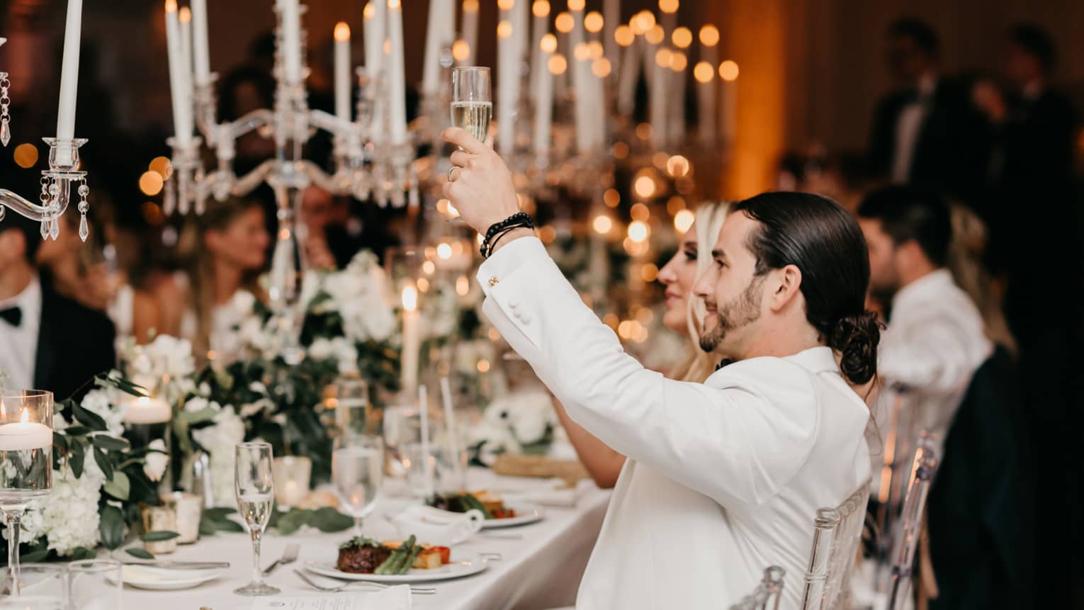 Wedding guests raise glasses during toast at candlelit banquet table