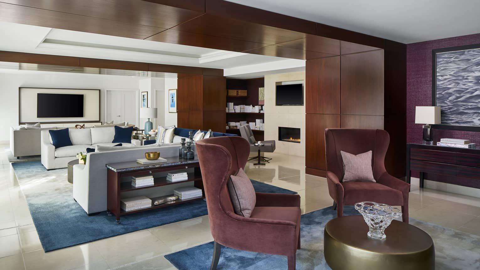 Sitting room with two maroon upholstered chairs, gold circular coffee table, connecting to light-filled living room