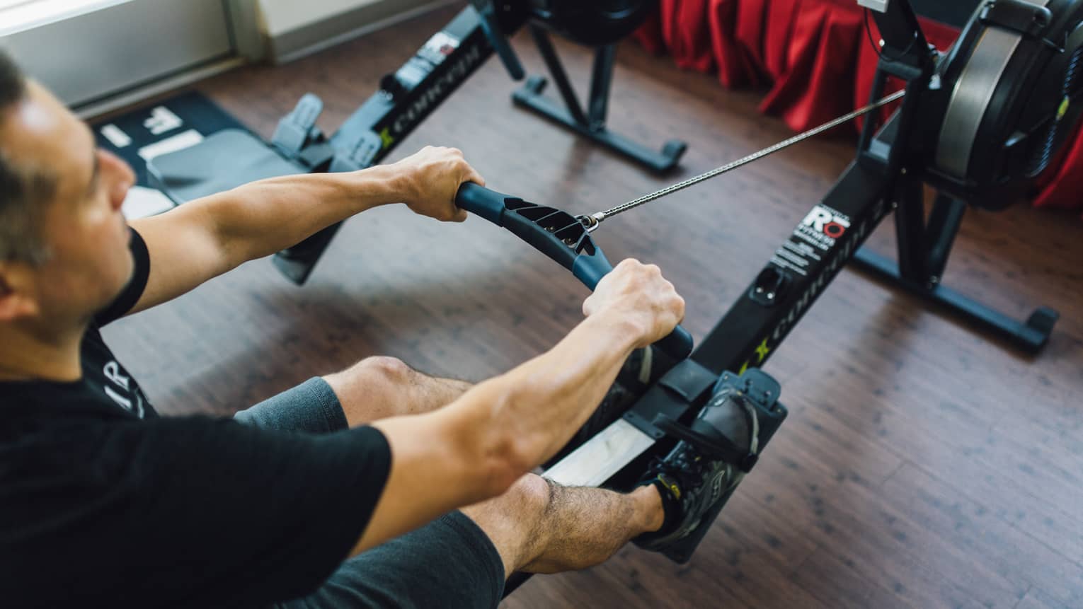 Man sits, pulls handle of cardio rowing machine in fitness facility