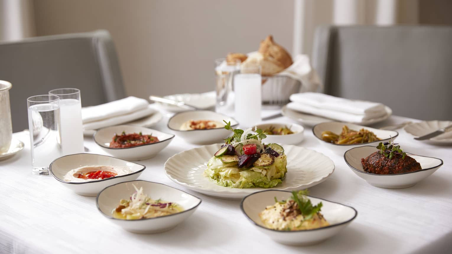 Small white dishes with lunch items, meats, breads, sauces on dining table