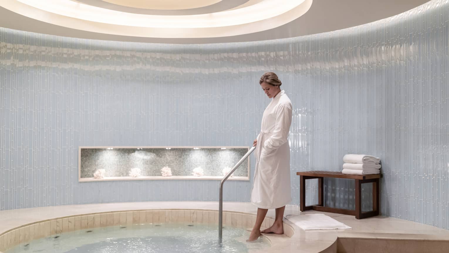 Woman wearing white robe steps into round spa hot tub