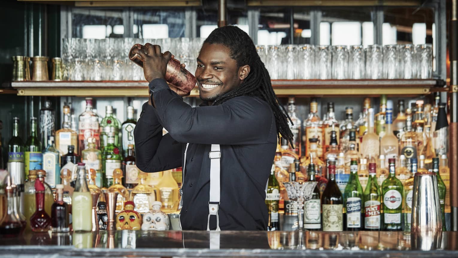 Smiling Butcher & Still bartender shakes cocktail behind bar, liquor display