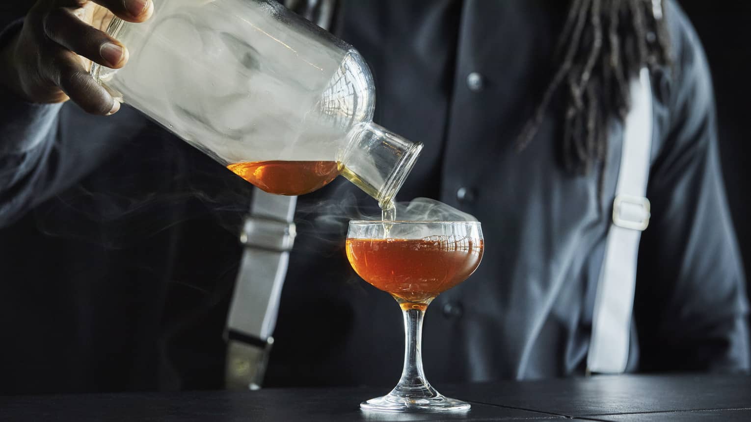 Smoke rolls off the decanter as a Four Seasons staff member pours bourbon into a coupe glass