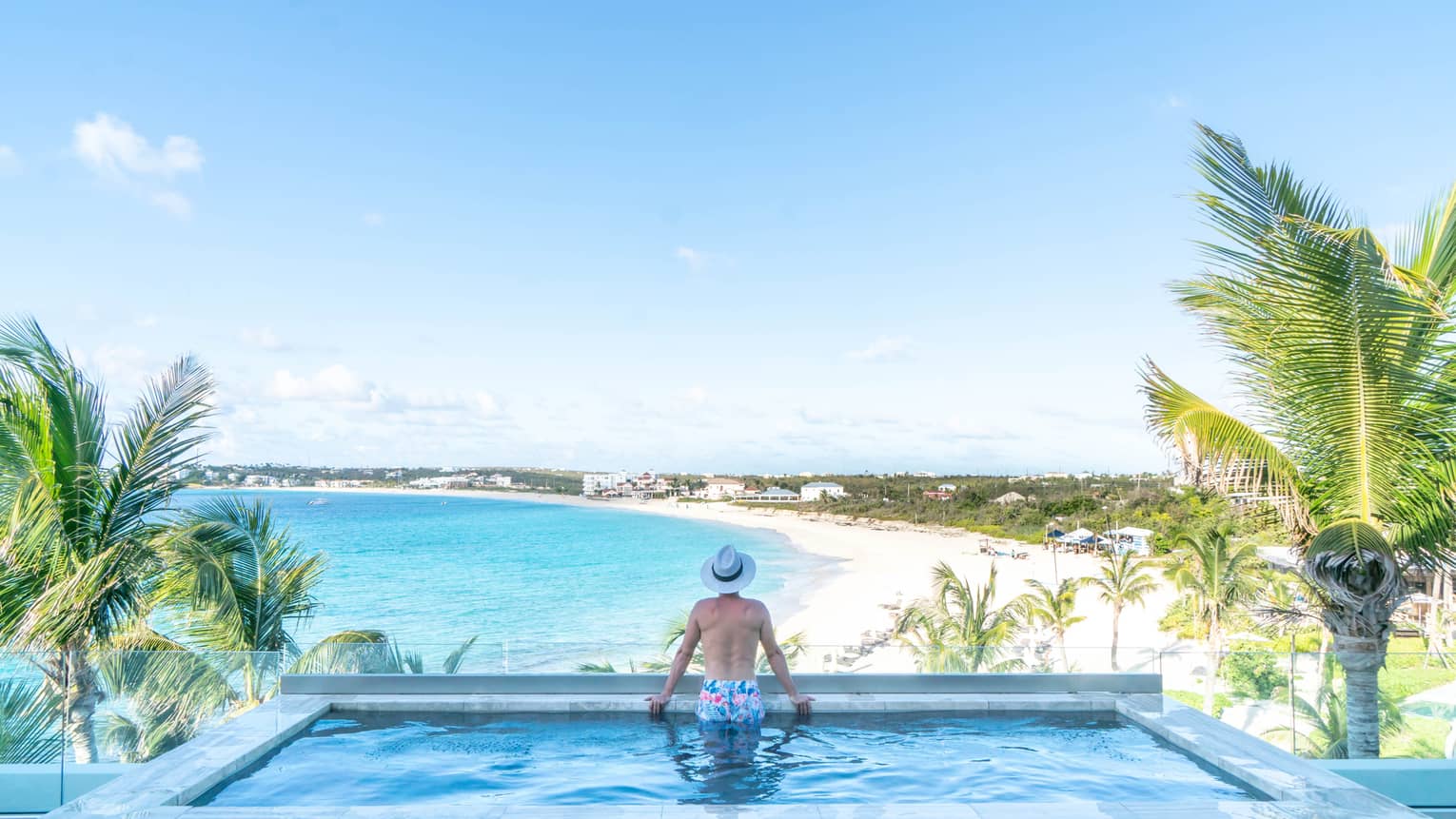 A man sitting at the edge of a pool looking across the ocean.