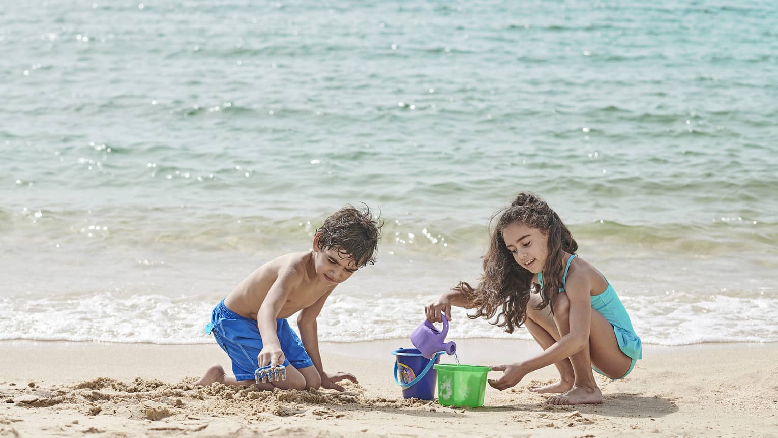 A little boy and little girl build a sandcastle on the beach at four seasons hotel alexandria