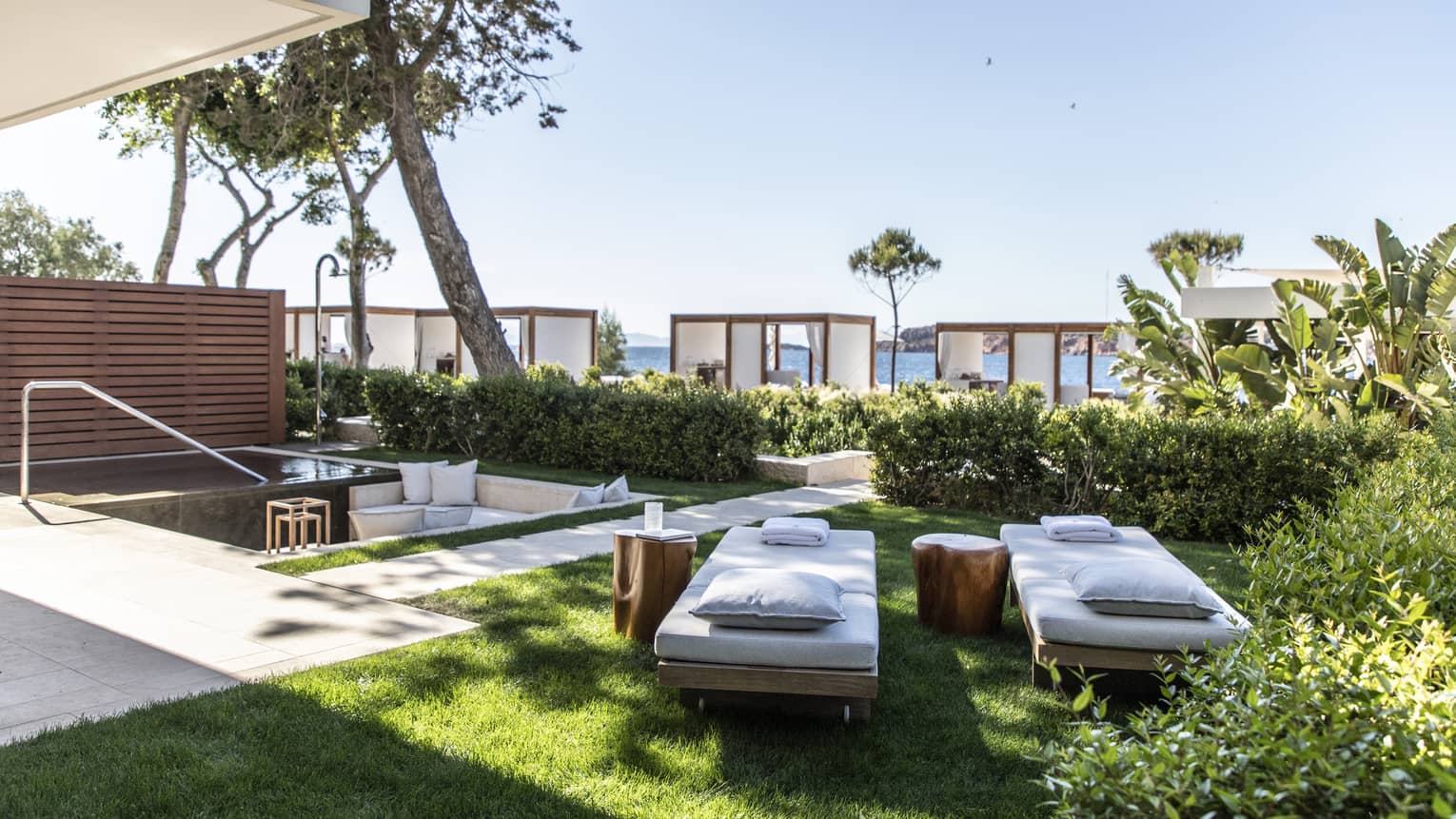 Private garden with two chaise lounges set on the grass, beach cabanas visible in the distance