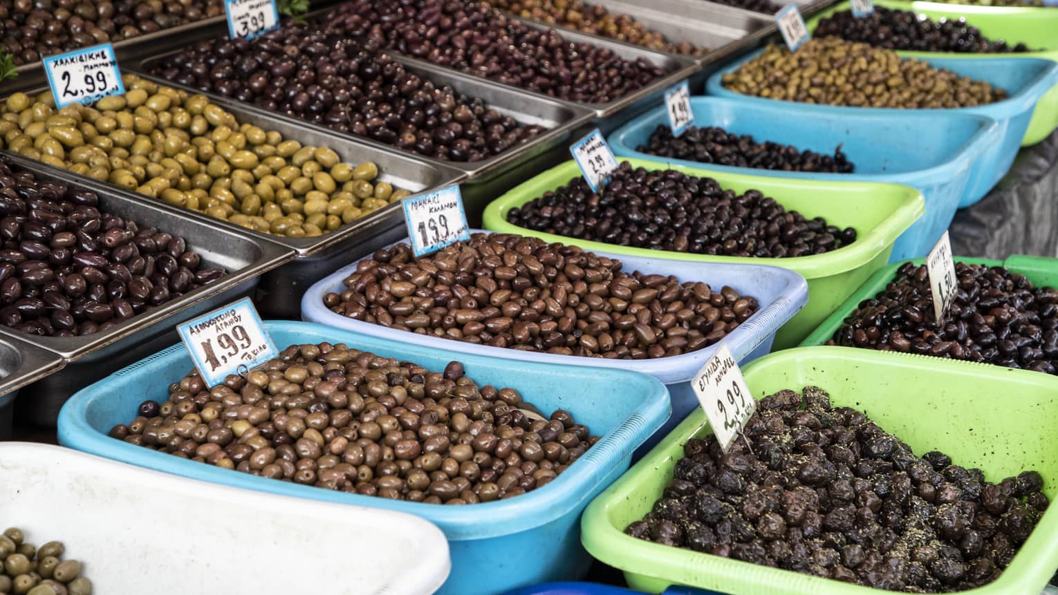 A wide assortment of olives displayed in rows of metal and plastic bins, each marked with the type of olive and the price.