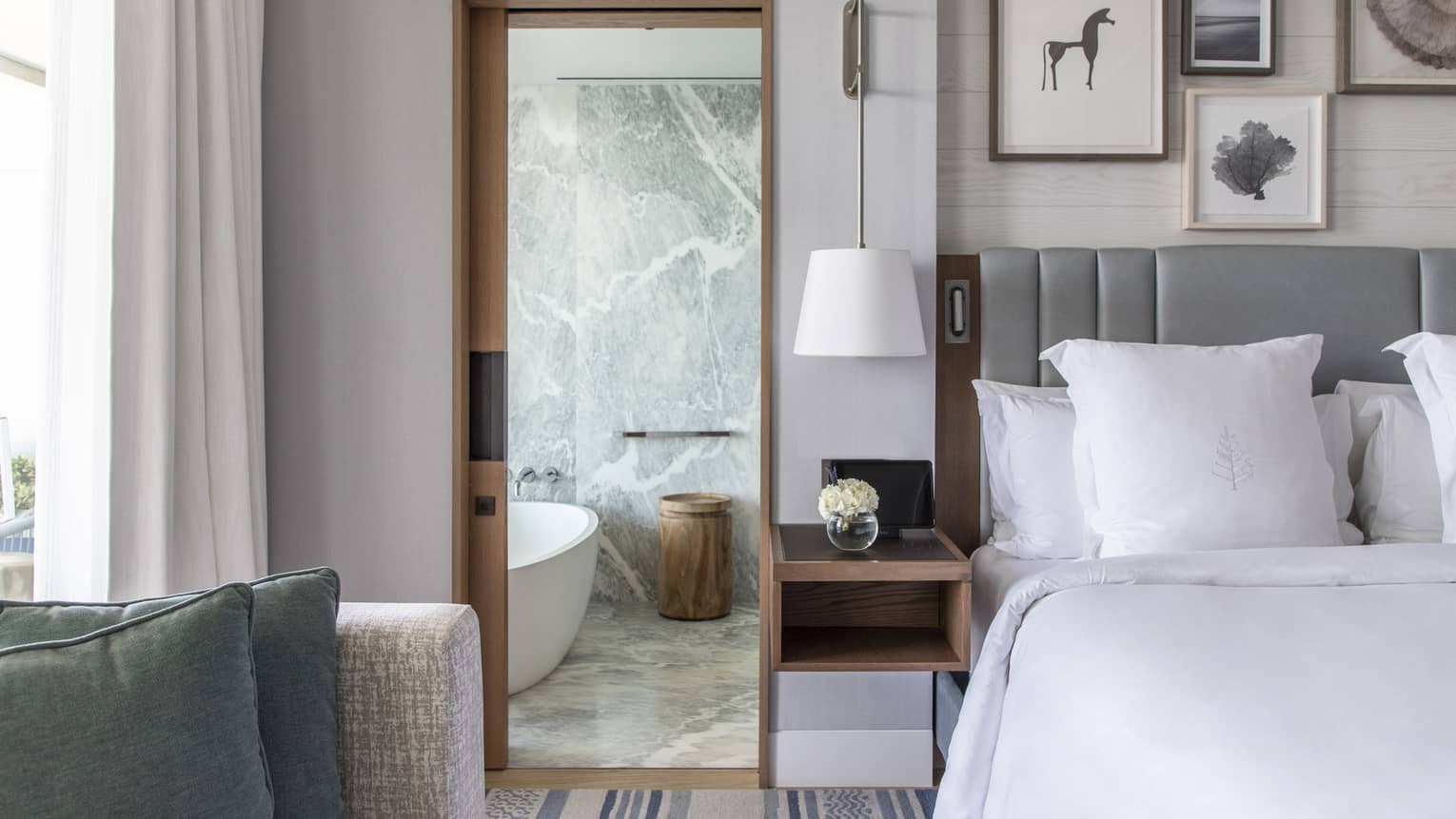 Bed, grey headboard, doorway to marble bathroom with tub
