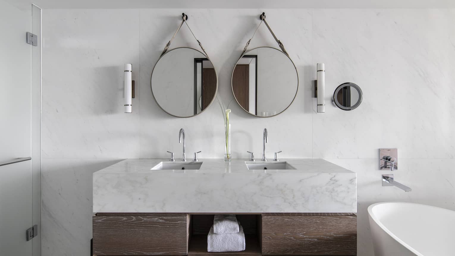 Bathroom with marble and wood vanity, two round mirrors, white tub