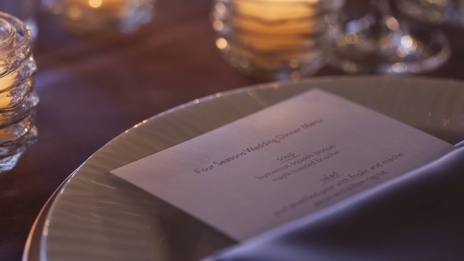 Close-up of wedding menu on dining plate near glowing candles