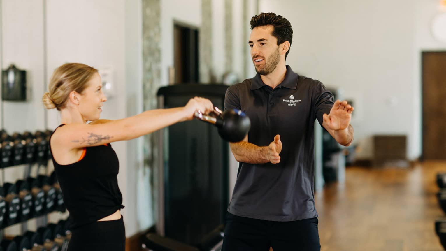Male fitness trainer works with female guest who is using a kettlebell