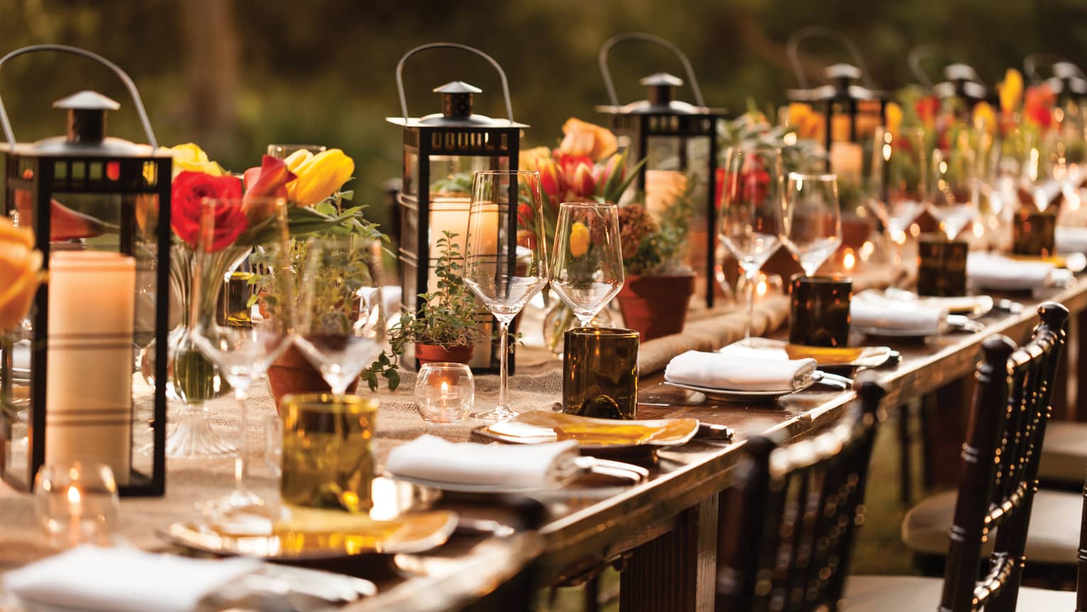 Close-up of long outdoor dining table set with lanterns, candles, wine glasses, flowers