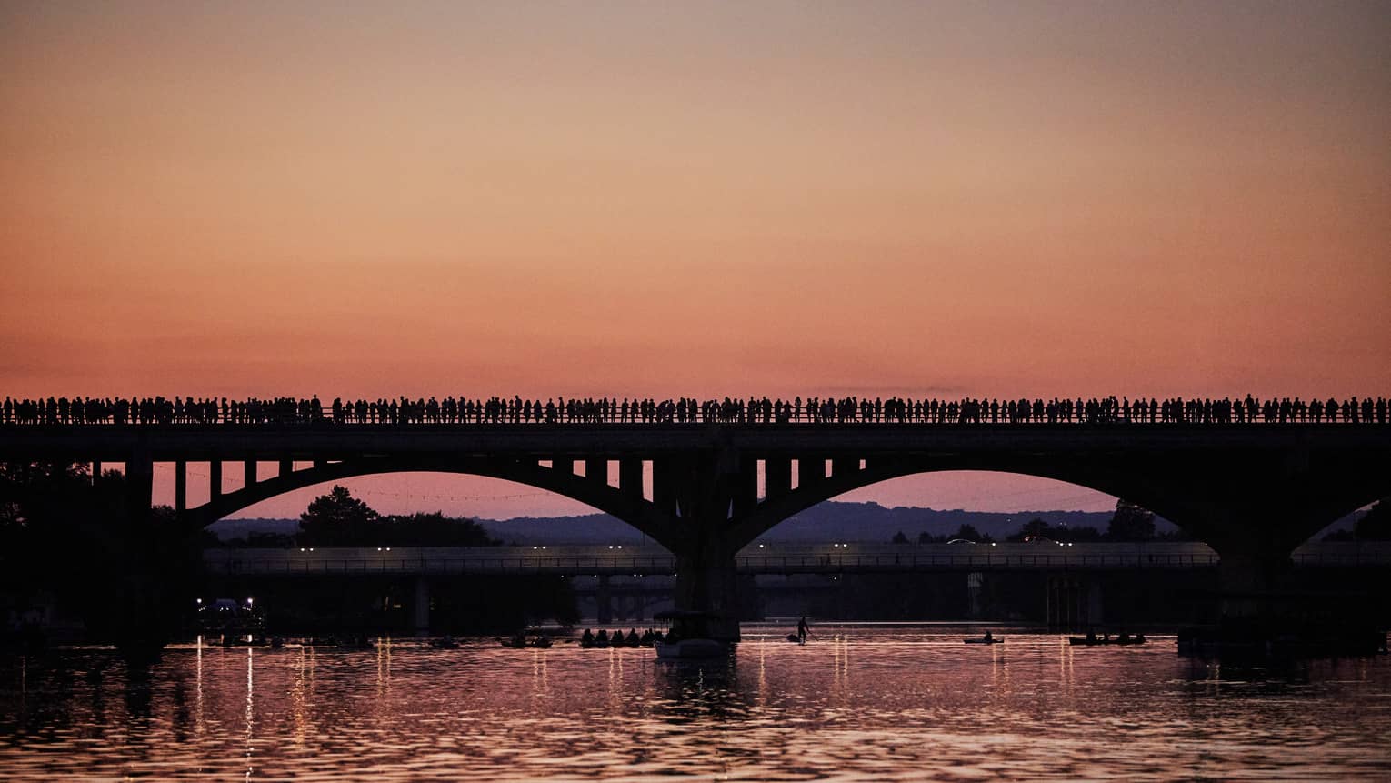 Silhouette of people lining long bridge over Lady Bird Lake at sunset