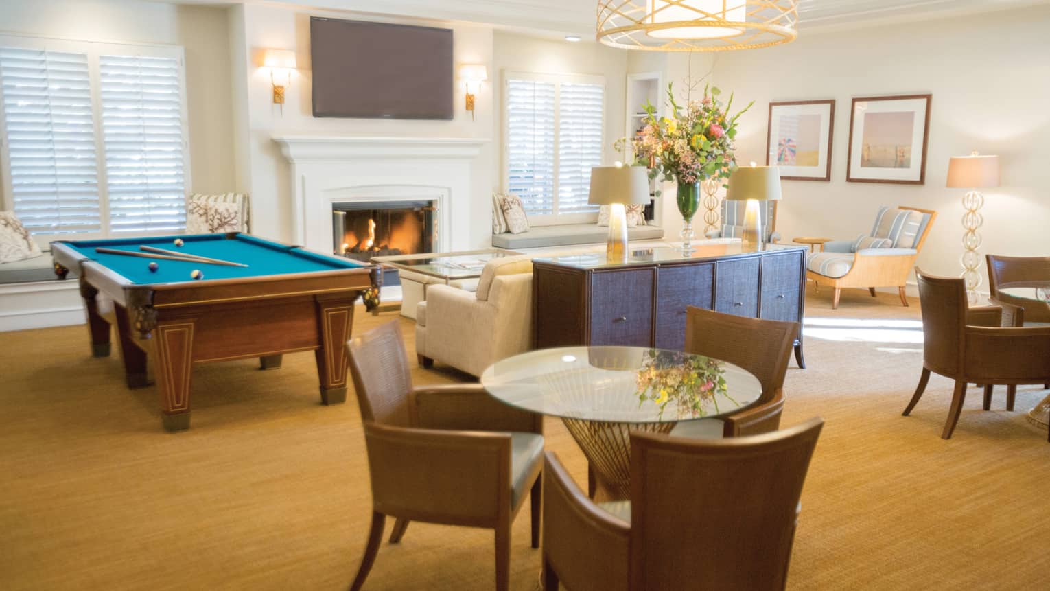 Hotel recreation lounge with pool table, fireplace and sofa, round glass tables with chairs 