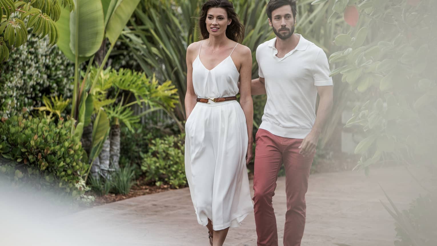 Man and woman in casual summer clothes stroll down path surrounded by tropical plants