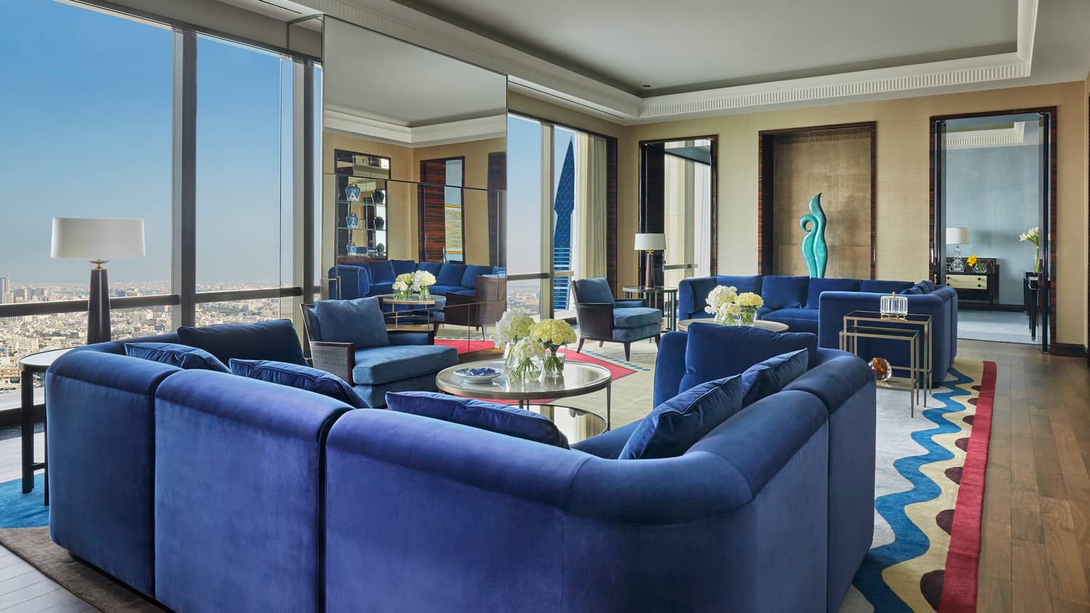 Royal Suite large u-shaped blue plush sofa, multiple seating areas, window with Bahrain city views