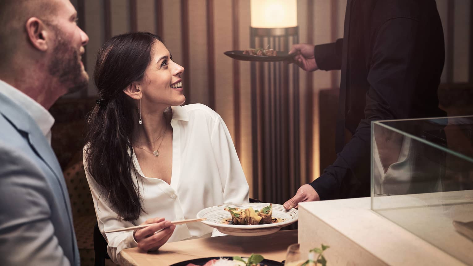 Two guests looking up at their waiter as they eat rice with chopsticks.