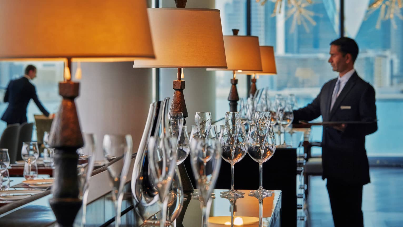 CUT by Wolfgang Puck restaurant sideboard lined with tall, shaded wooden lamps and champagne flutes, staff in background