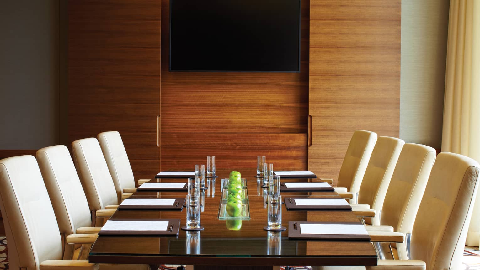 Boardroom meeting table set with green apples, water glasses and lined with white leather chairs 