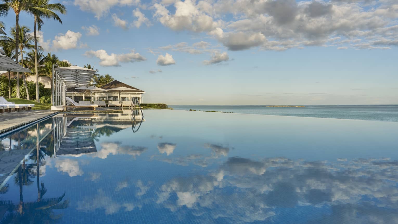 A building on the shore with clouds reflecting in the ocean water.