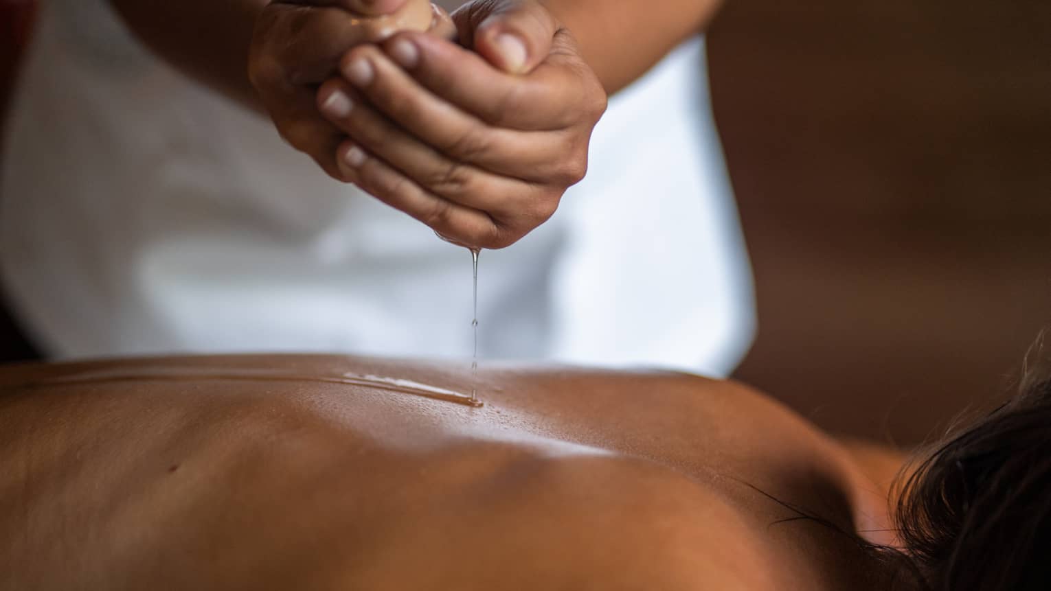 Delicate hands apply oil to a guest's back during a spa treatment