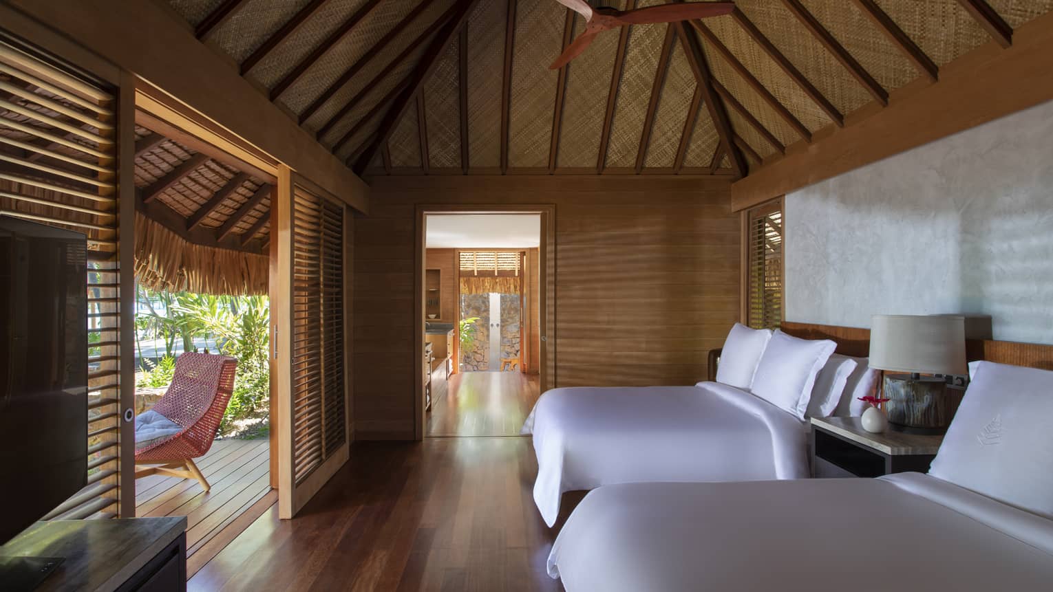 Two queen beds in a villa, with teak floors, a thatched roof and a walk-out patio
