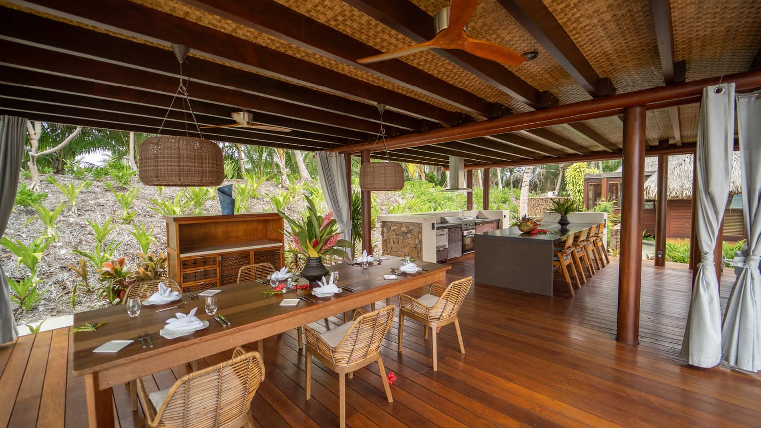 Open-air dining area with wooden floors, bamboo chairs, thatch roof
