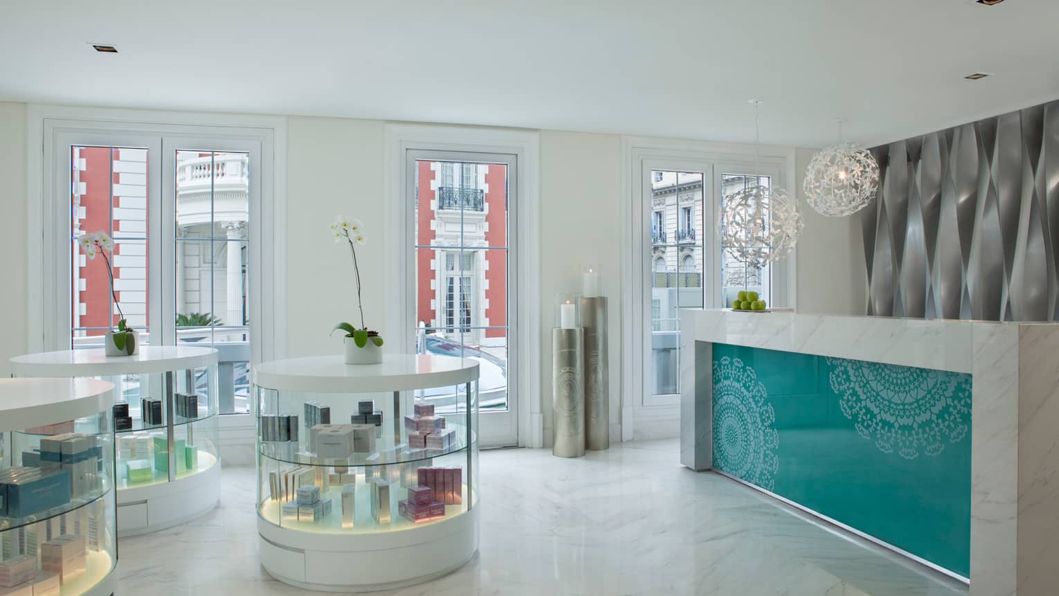 White marble spa lobby with round glass display cabinets, desk with teal pattern, white lamp