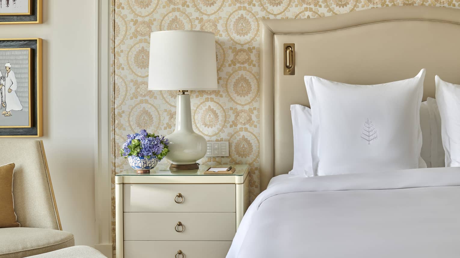 Bed with white sheets and Four Seasons-embroidered sham, nightstand and lamp