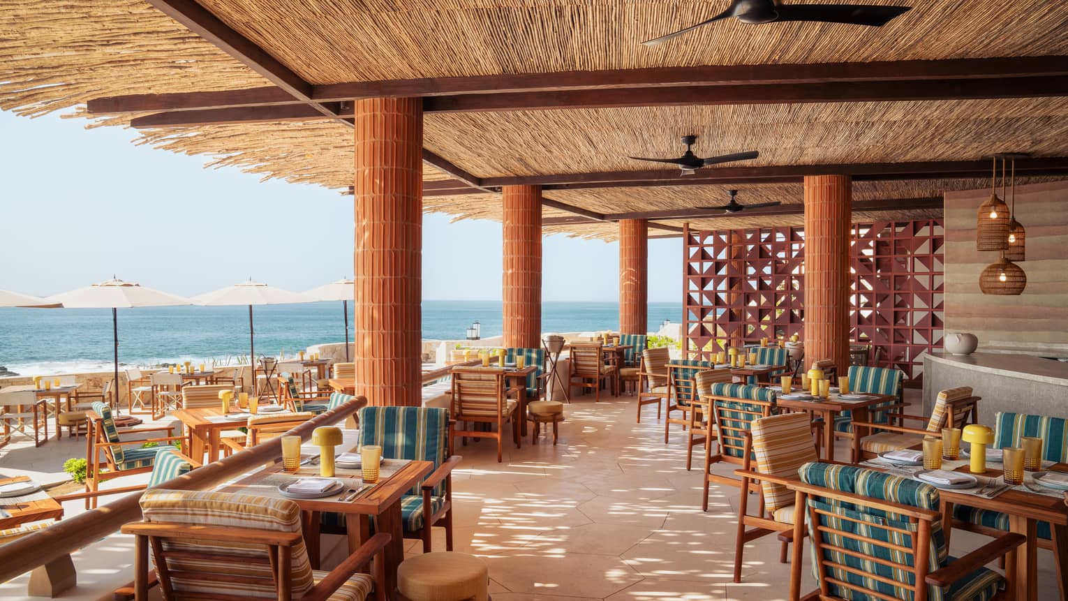 Outdoor restaurant terrace under a straw roof with ocean view, at Four Seasons Resort and Residences Cabo San Lucas