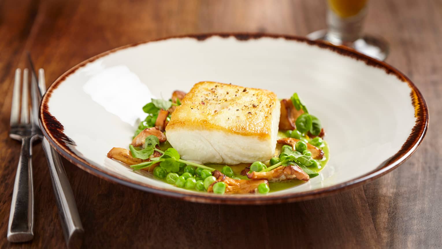 Pan-roasted Alaskan halibut fillet on fresh green peas, herbs and mushrooms in bowl