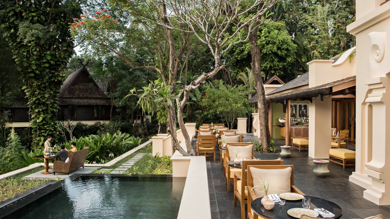 KHAO slate patio under shade of trees, long fountain by dining tables near large white columns