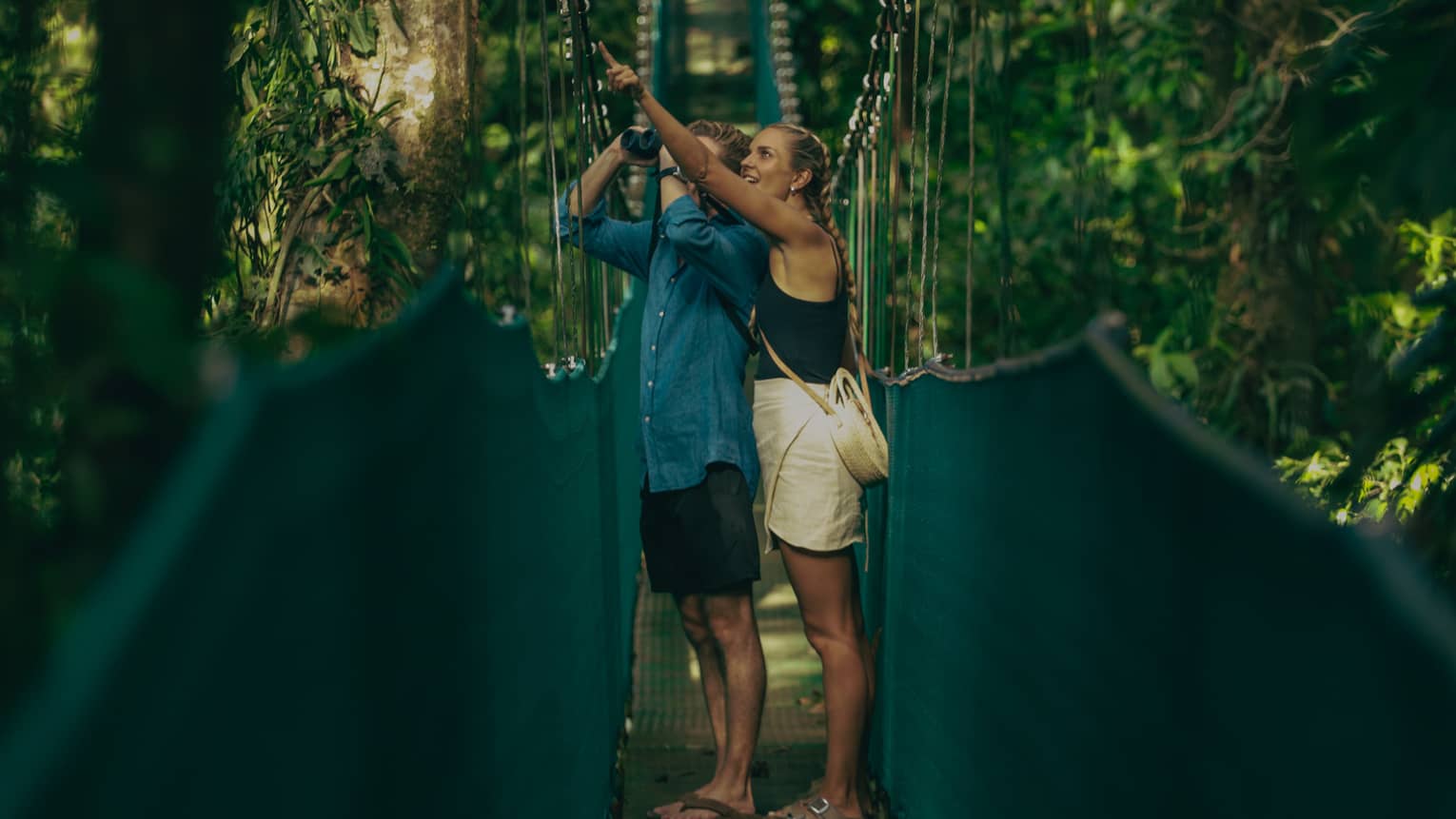 A man and woman walking along a hanging bridge.