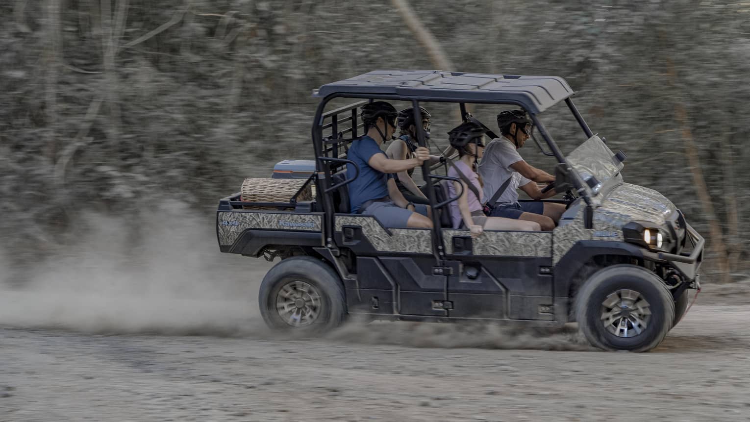 Four people speed along a dirt road in a 4x4 vehicle