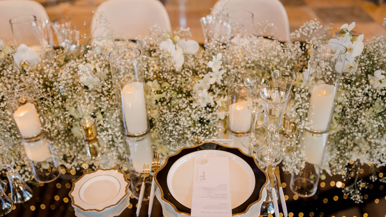 Closeup of table set for wedding reception with white flowers, candles, chair covers and dishes