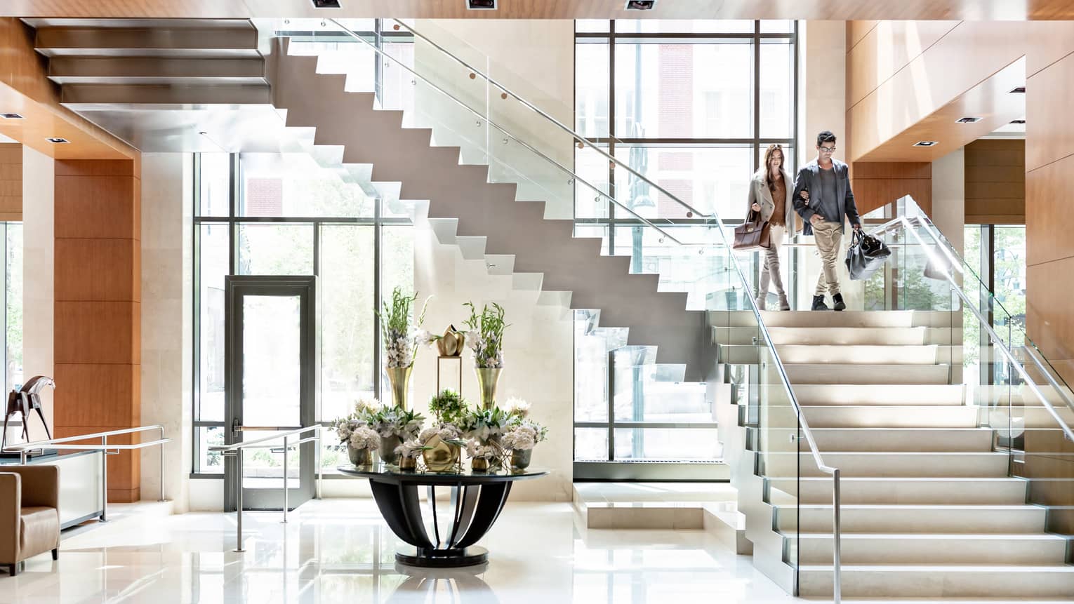 Two people walk down staircase in light-filled hotel lobby