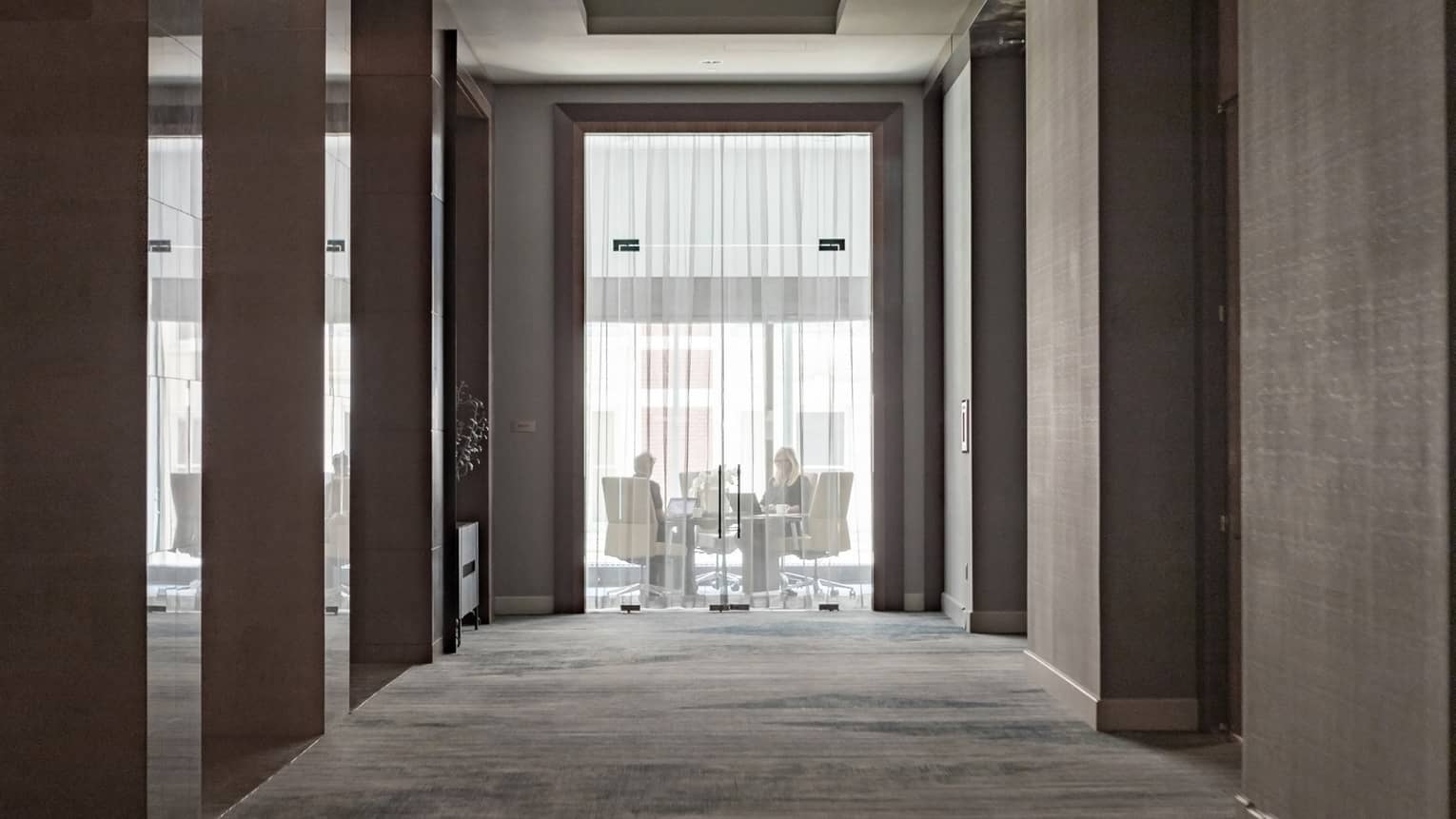 A see-through curtain with two people working at a table with comfortable chairs behind it.