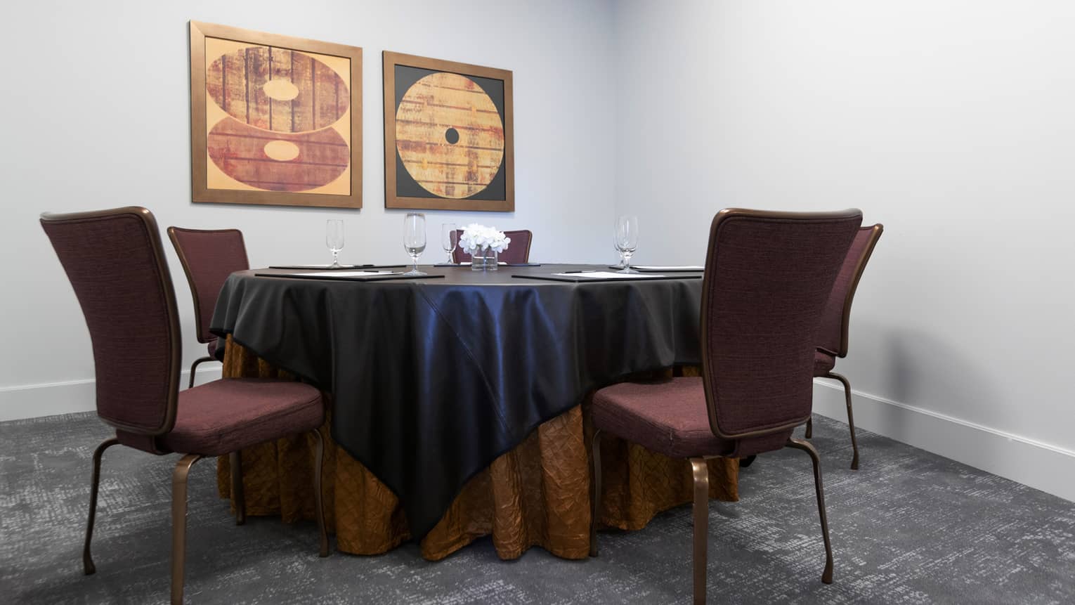 A round meeting table surrounded by four chairs, with two pieces of art on the wall.