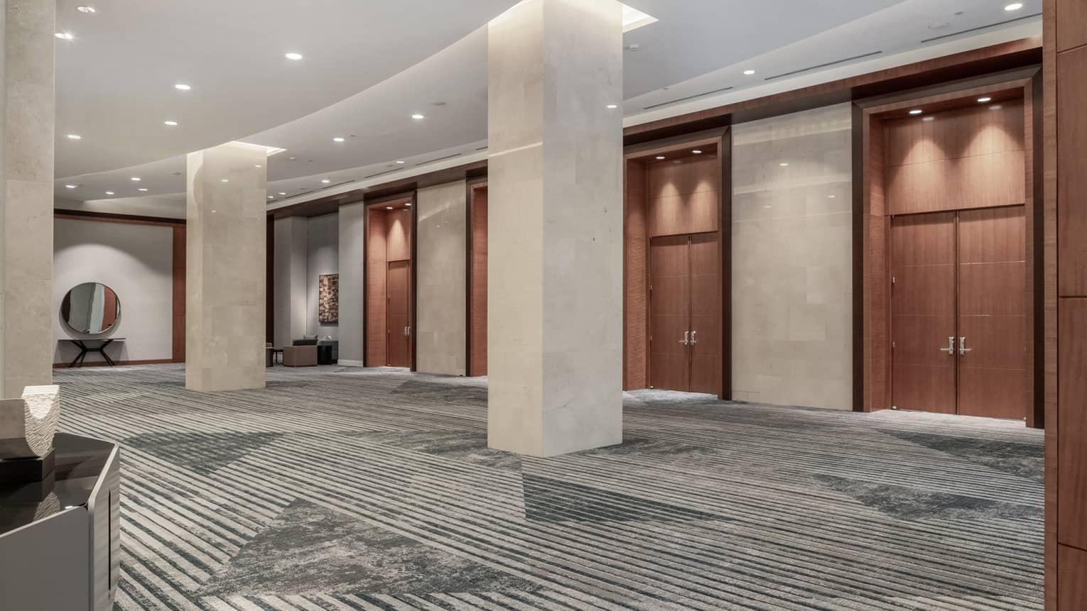 A large lobby meeting area with a series of large wooden doors and pillars.