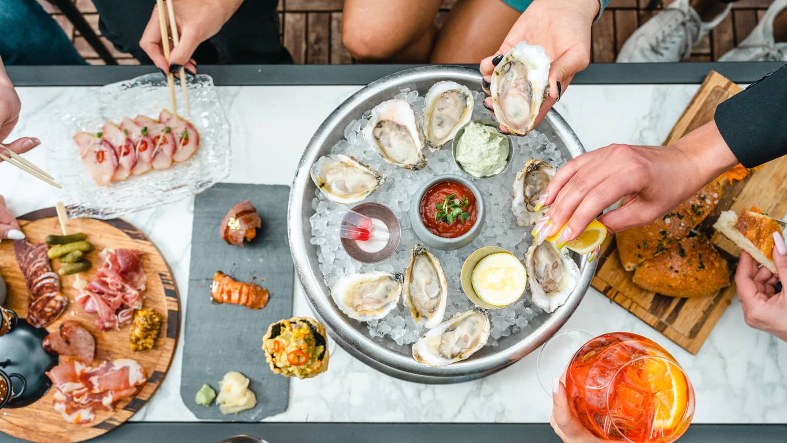 Looking down at a table with various people sharing an oyster-on-ice platter and other appetizers