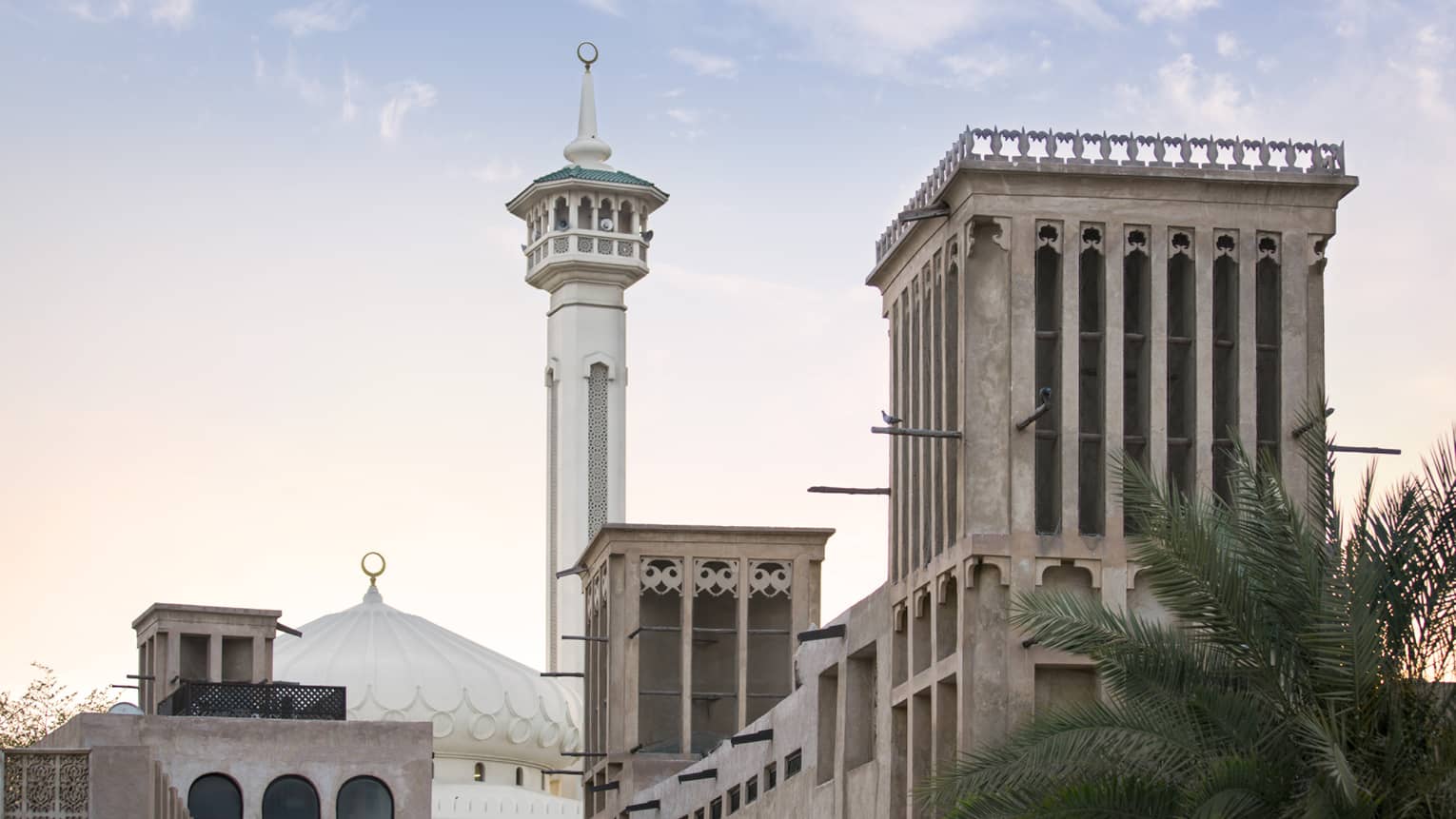 Street view of a mosque with a domed roof and adjoining minaret; in the fore, adobe buildings featuring ornate wind towers.